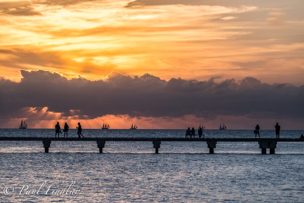 Silhouetted people on pier at sunset.