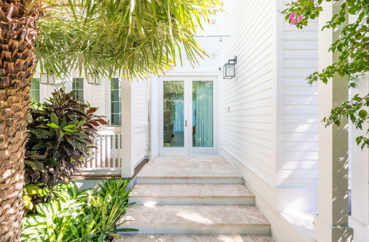 Inviting pathway leading to a glass door entrance, surrounded by lush greenery and palm trees.